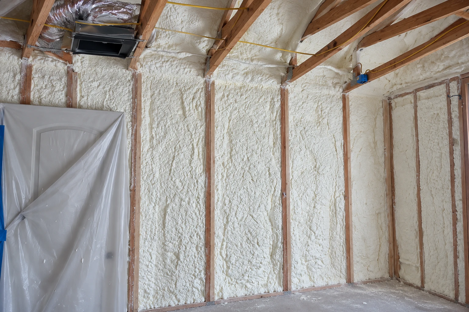 Open-cell spray foam fills the walls and ceiling between exposed wooden framing in an unfinished room.