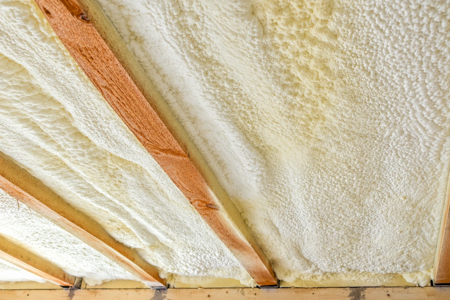 White spray foam insulation fills the spaces between exposed wooden roof rafters.